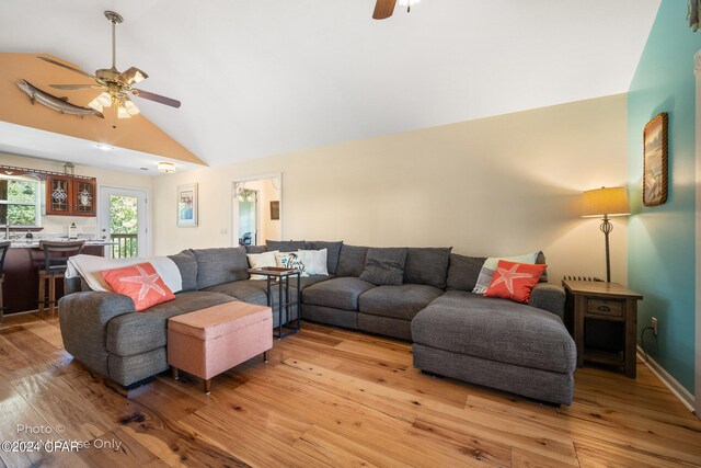 living room with ceiling fan, light hardwood / wood-style floors, and vaulted ceiling