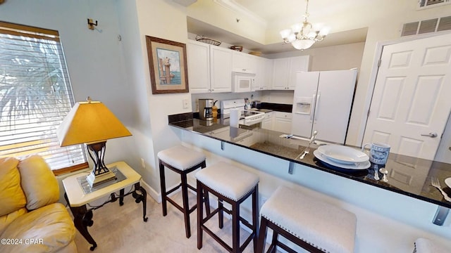 kitchen with white appliances, a breakfast bar area, kitchen peninsula, hanging light fixtures, and white cabinets