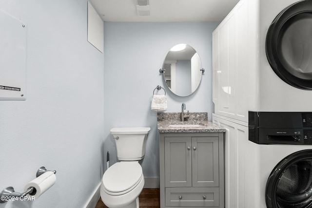 bathroom featuring stacked washer and clothes dryer, vanity, and toilet