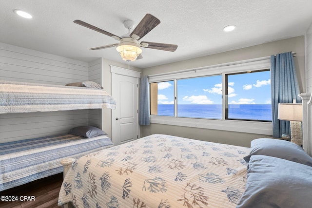 bedroom with ceiling fan, a textured ceiling, a closet, dark hardwood / wood-style floors, and a water view