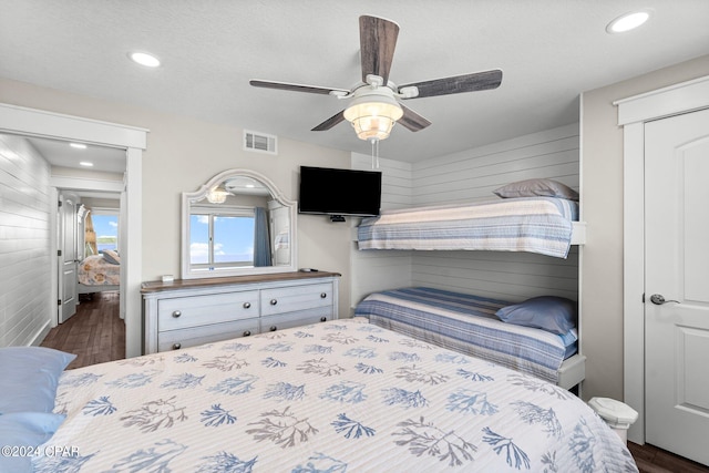 bedroom featuring a textured ceiling, dark hardwood / wood-style floors, wooden walls, and ceiling fan