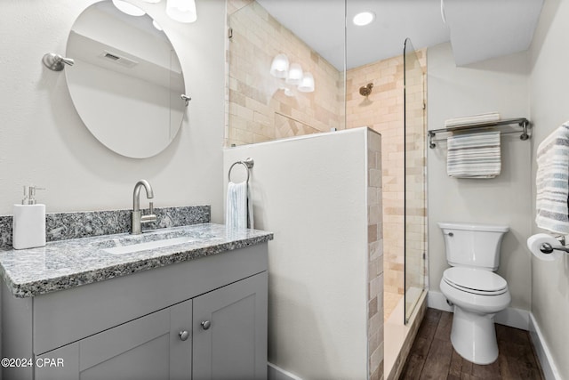 bathroom with wood-type flooring, a tile shower, vanity, and toilet