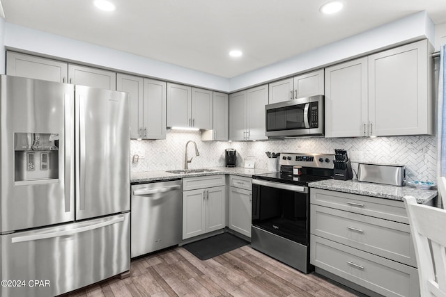 kitchen featuring light stone counters, stainless steel appliances, tasteful backsplash, sink, and dark hardwood / wood-style flooring