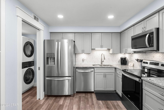 kitchen featuring sink, stacked washer / dryer, appliances with stainless steel finishes, dark hardwood / wood-style floors, and light stone countertops