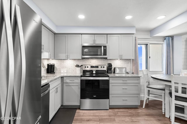 kitchen with wood-type flooring, light stone countertops, gray cabinets, and appliances with stainless steel finishes