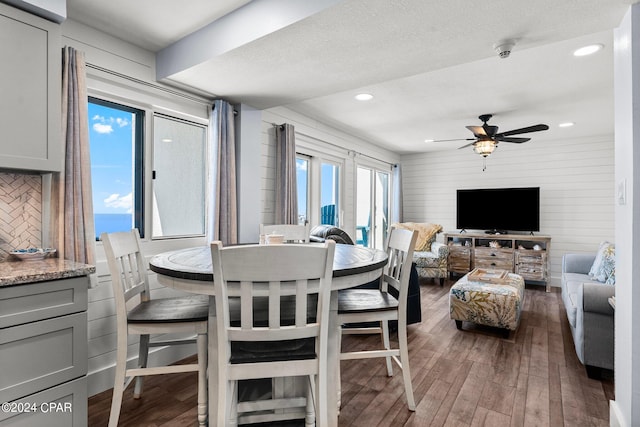 dining space featuring hardwood / wood-style flooring, wooden walls, ceiling fan, and a textured ceiling