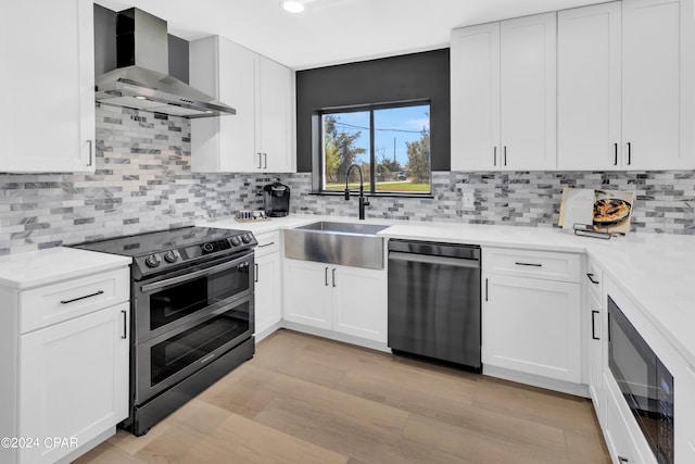 kitchen with decorative backsplash, stainless steel appliances, white cabinets, wall chimney exhaust hood, and sink