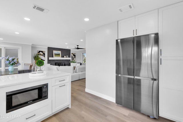 kitchen with stainless steel fridge, a brick fireplace, light hardwood / wood-style flooring, white cabinetry, and black microwave