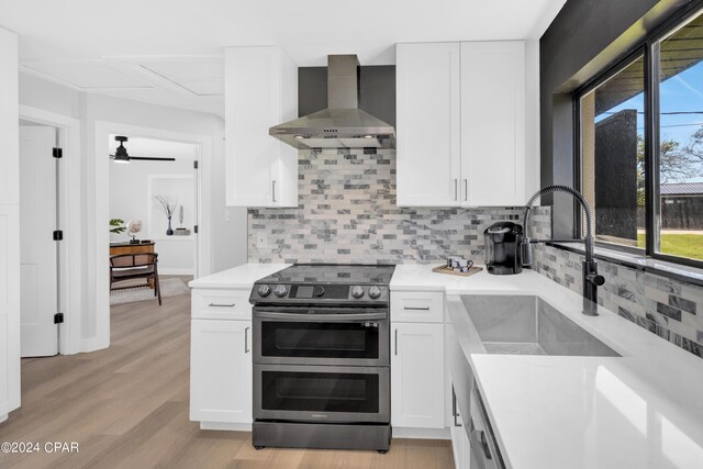 kitchen featuring wall chimney exhaust hood, light hardwood / wood-style flooring, sink, double oven range, and white cabinets