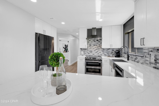 kitchen with light stone counters, stainless steel appliances, sink, wall chimney range hood, and white cabinetry