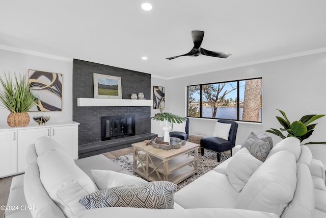 living room featuring ceiling fan, light hardwood / wood-style flooring, a fireplace, crown molding, and a water view