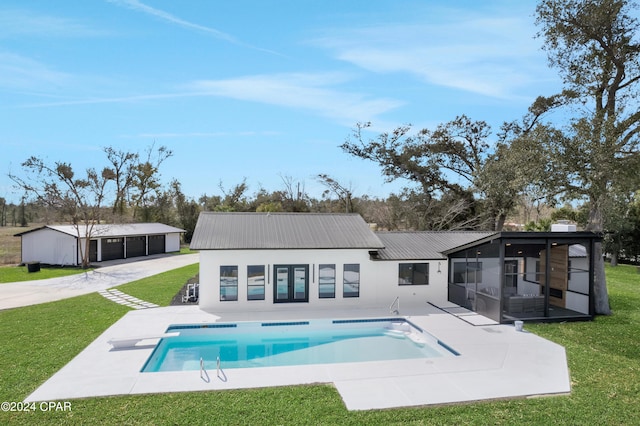 back of property featuring an outdoor structure, a yard, a sunroom, and a patio area