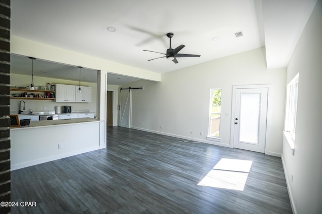 unfurnished living room with a barn door, baseboards, visible vents, a ceiling fan, and dark wood-type flooring