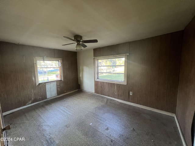 empty room featuring a wealth of natural light, ceiling fan, and wood walls