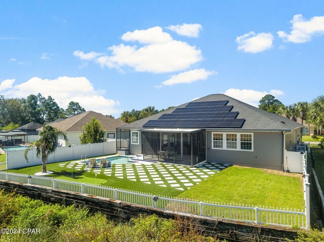 back of property with a fenced in pool, a sunroom, a patio area, solar panels, and a lawn