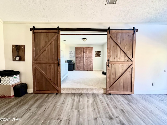 interior space featuring a barn door, ornamental molding, light wood-type flooring, and a textured ceiling