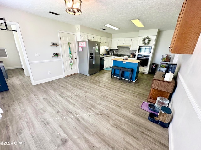 kitchen featuring light wood-type flooring, black appliances, a center island, white cabinetry, and a kitchen breakfast bar