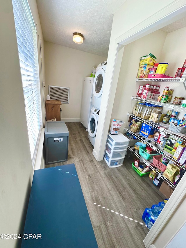 laundry area featuring hardwood / wood-style floors, stacked washer / dryer, and a textured ceiling