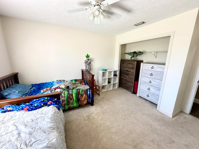 bedroom with a closet, light colored carpet, a textured ceiling, and ceiling fan