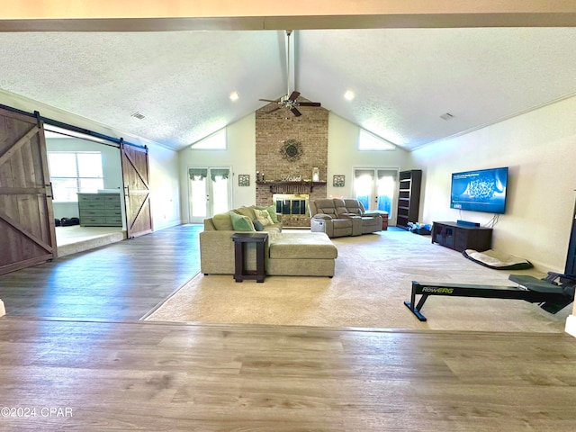 unfurnished living room featuring ceiling fan, a textured ceiling, a barn door, a fireplace, and hardwood / wood-style floors