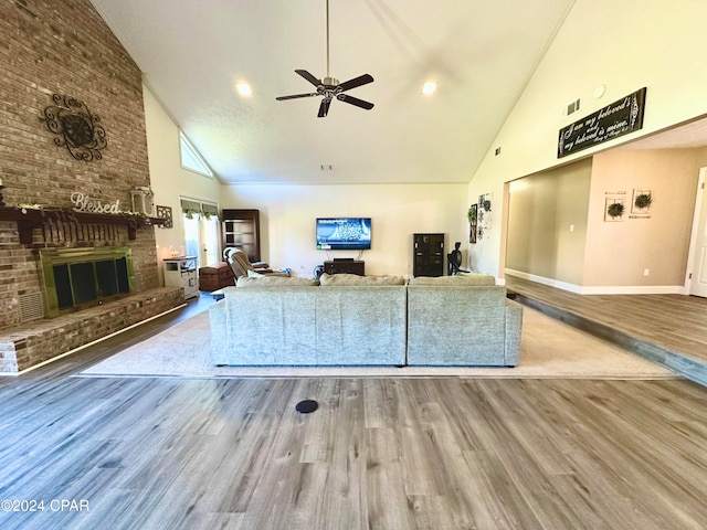 unfurnished living room with a brick fireplace, hardwood / wood-style flooring, high vaulted ceiling, and ceiling fan