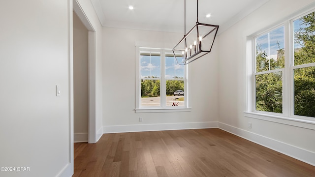 unfurnished dining area featuring an inviting chandelier, plenty of natural light, crown molding, and hardwood / wood-style flooring