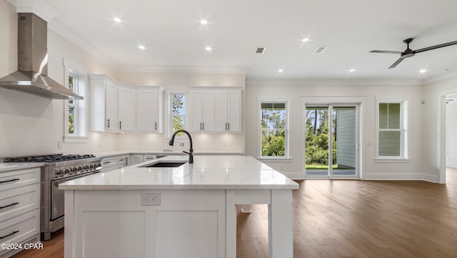 kitchen featuring wall chimney range hood, a kitchen island with sink, wood-type flooring, light stone counters, and high end stainless steel range oven