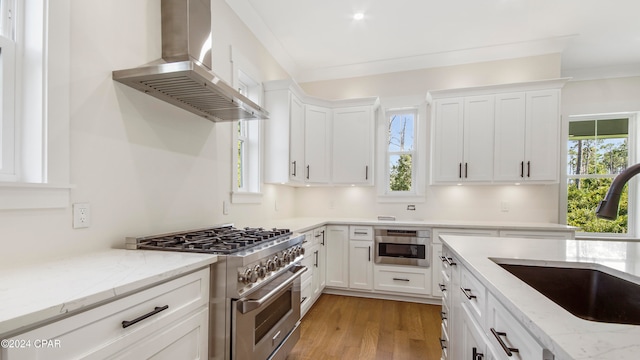 kitchen featuring wall chimney exhaust hood, white cabinets, appliances with stainless steel finishes, and sink