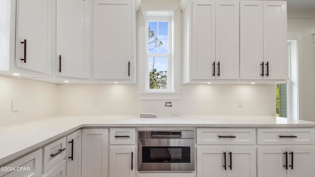 kitchen featuring stainless steel oven, white cabinets, light stone counters, and a healthy amount of sunlight