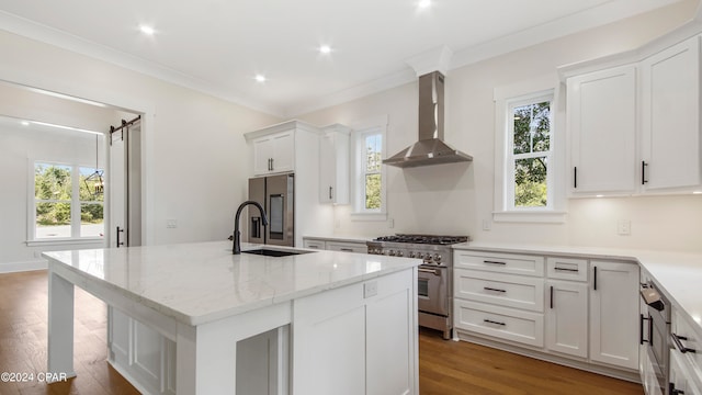 kitchen featuring an island with sink, wall chimney exhaust hood, white cabinetry, hardwood / wood-style flooring, and appliances with stainless steel finishes