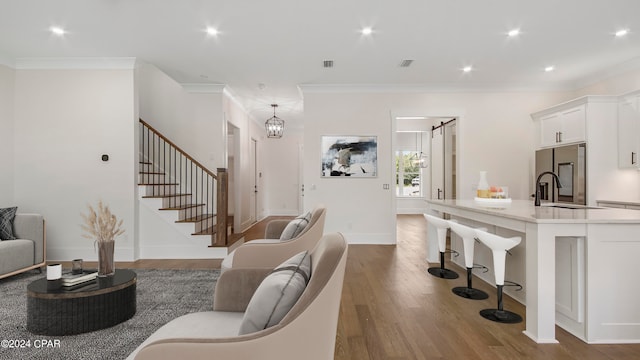 living room featuring a notable chandelier, ornamental molding, sink, and hardwood / wood-style floors