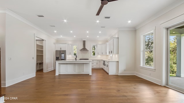 kitchen with wall chimney exhaust hood, plenty of natural light, a kitchen island with sink, and stainless steel refrigerator with ice dispenser