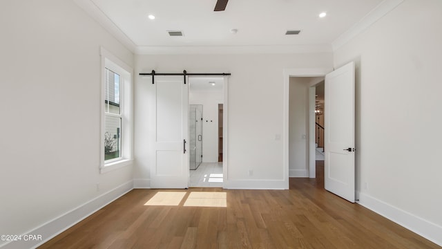 unfurnished bedroom featuring a barn door, crown molding, hardwood / wood-style flooring, and multiple windows