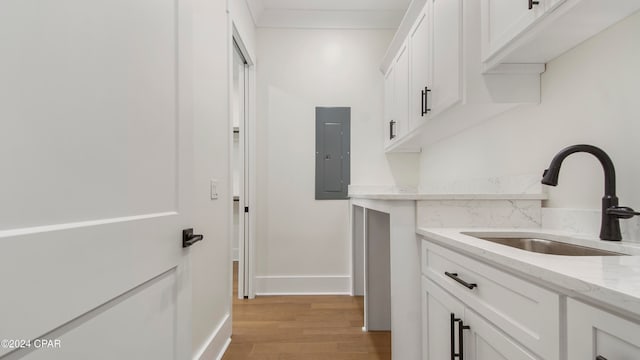 clothes washing area with electric panel, light hardwood / wood-style floors, and sink