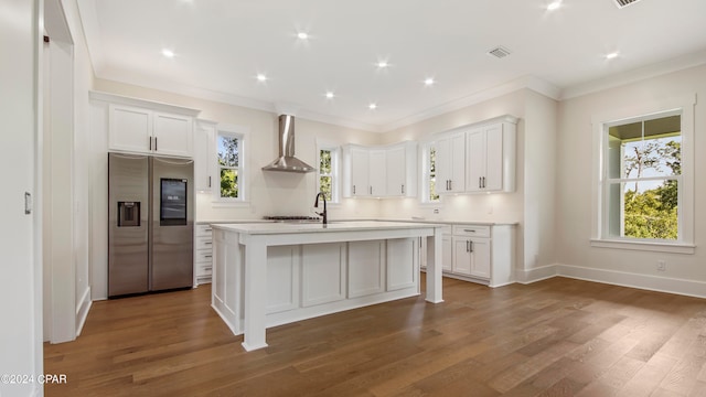 kitchen featuring stainless steel refrigerator with ice dispenser, wall chimney exhaust hood, white cabinetry, and an island with sink