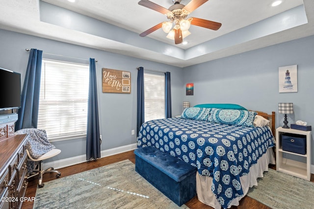 bedroom featuring ceiling fan, dark hardwood / wood-style floors, and a tray ceiling