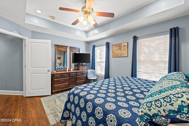 bedroom with dark wood-type flooring, a tray ceiling, and ceiling fan