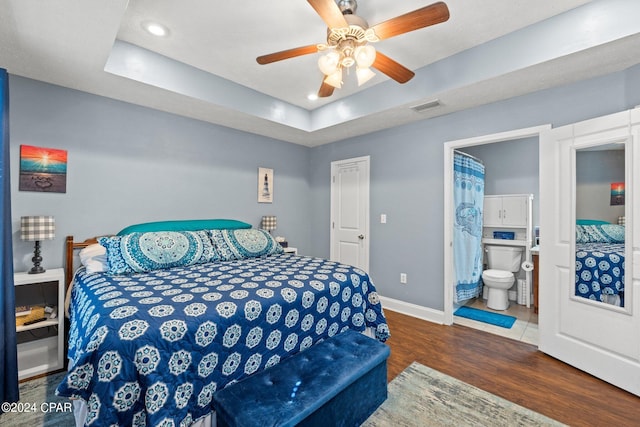 bedroom featuring dark wood-type flooring, a raised ceiling, ceiling fan, and ensuite bathroom