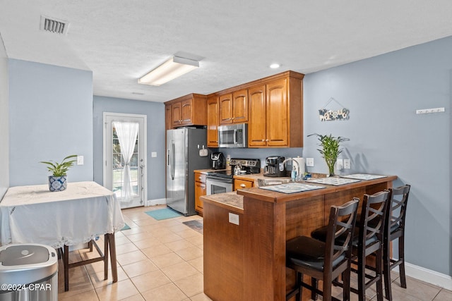 kitchen featuring stainless steel appliances, light tile patterned flooring, kitchen peninsula, a kitchen bar, and a textured ceiling