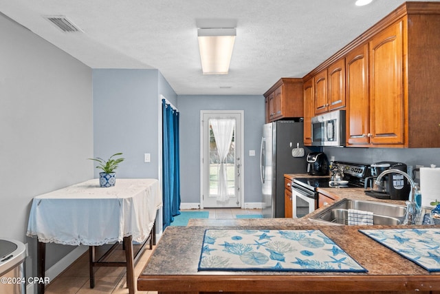 kitchen featuring stainless steel appliances, light tile patterned flooring, a textured ceiling, and sink