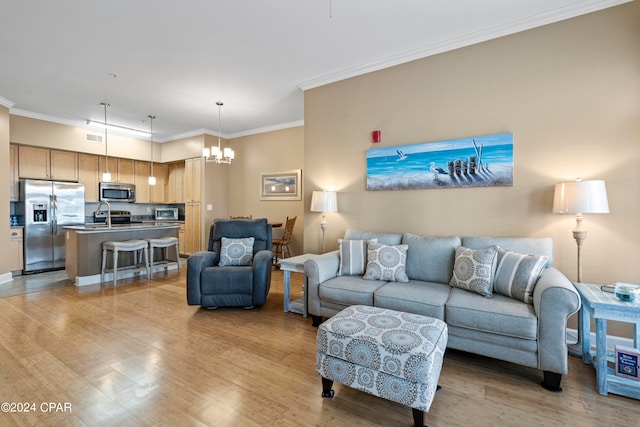 living room with light hardwood / wood-style floors, sink, crown molding, and a chandelier