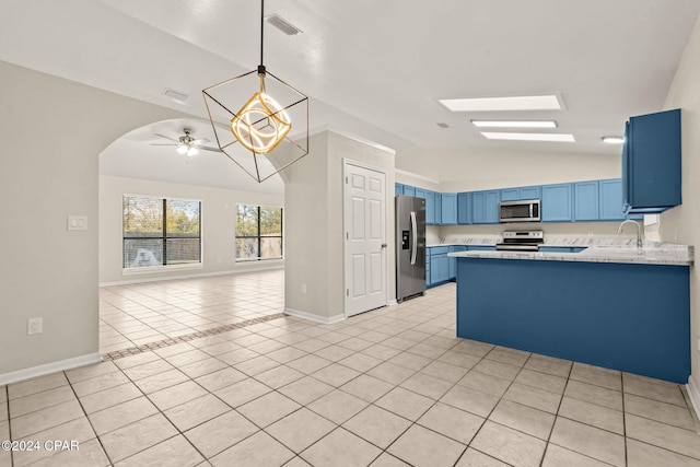 kitchen featuring kitchen peninsula, blue cabinets, lofted ceiling with skylight, light tile patterned floors, and appliances with stainless steel finishes