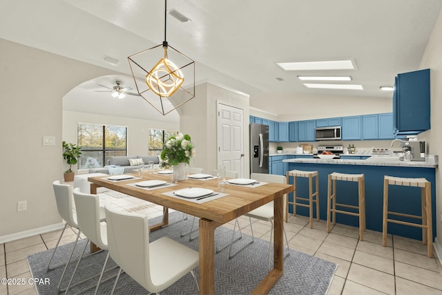 tiled dining area with vaulted ceiling with skylight and ceiling fan with notable chandelier