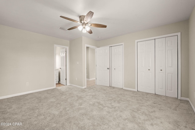 unfurnished bedroom with ceiling fan, light colored carpet, connected bathroom, and multiple closets