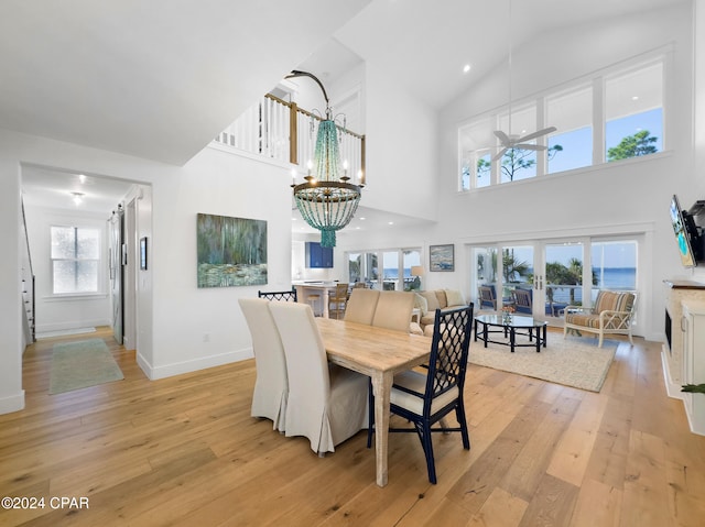 dining area featuring ceiling fan with notable chandelier, light hardwood / wood-style floors, high vaulted ceiling, and a healthy amount of sunlight