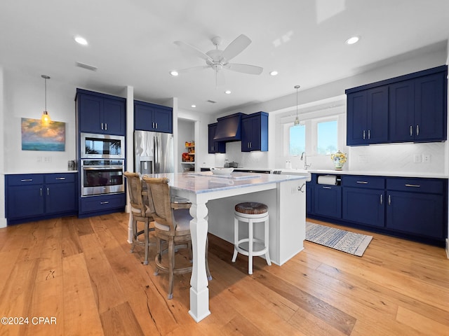 kitchen with a kitchen bar, appliances with stainless steel finishes, light hardwood / wood-style flooring, and hanging light fixtures