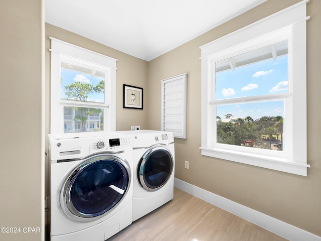 clothes washing area featuring plenty of natural light, light hardwood / wood-style flooring, and washing machine and clothes dryer