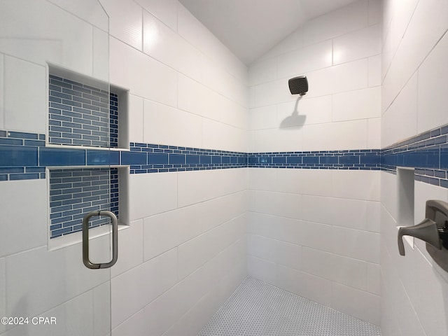 bathroom featuring a shower with door, lofted ceiling, and tile walls