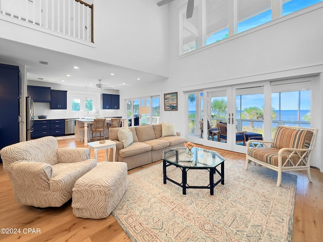 living room featuring a healthy amount of sunlight, a water view, a high ceiling, and light hardwood / wood-style flooring