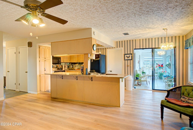 kitchen with light brown cabinets, kitchen peninsula, black appliances, ceiling fan with notable chandelier, and light wood-type flooring